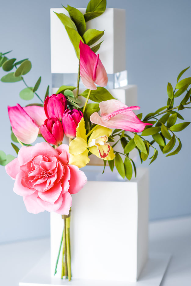A white square cake with pink and yellow flowers with a 30mm Square Acrylic Cake Separator between each layer - Prop Options