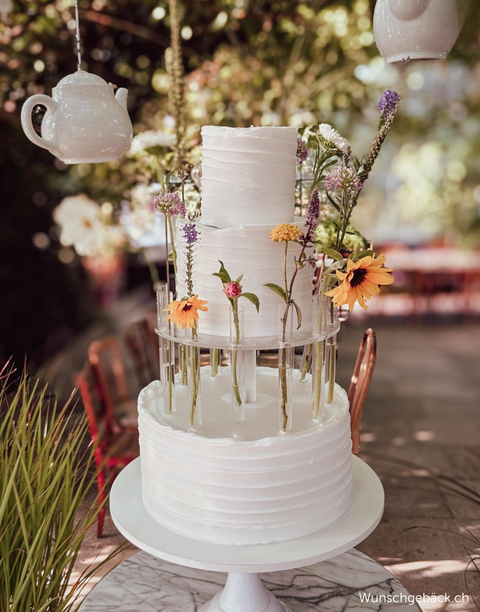 Outdoor wedding cake displayed with Prop Options Floral Tiara cake separator in a garden setting