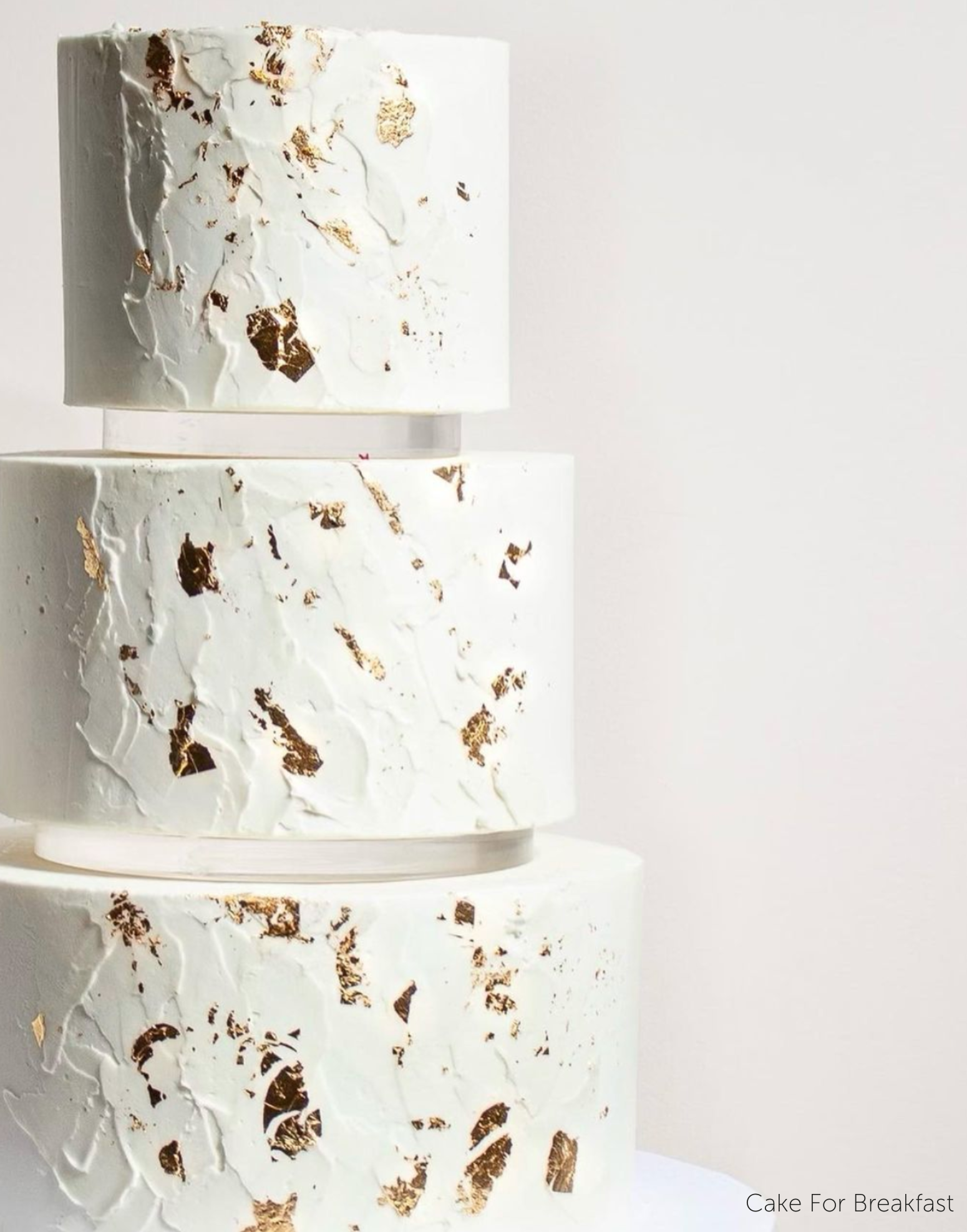 A plain white three tier cake with subtle gold decorations, each layer is separated by a 15mm Acrylic Cake Separator - Prop Options