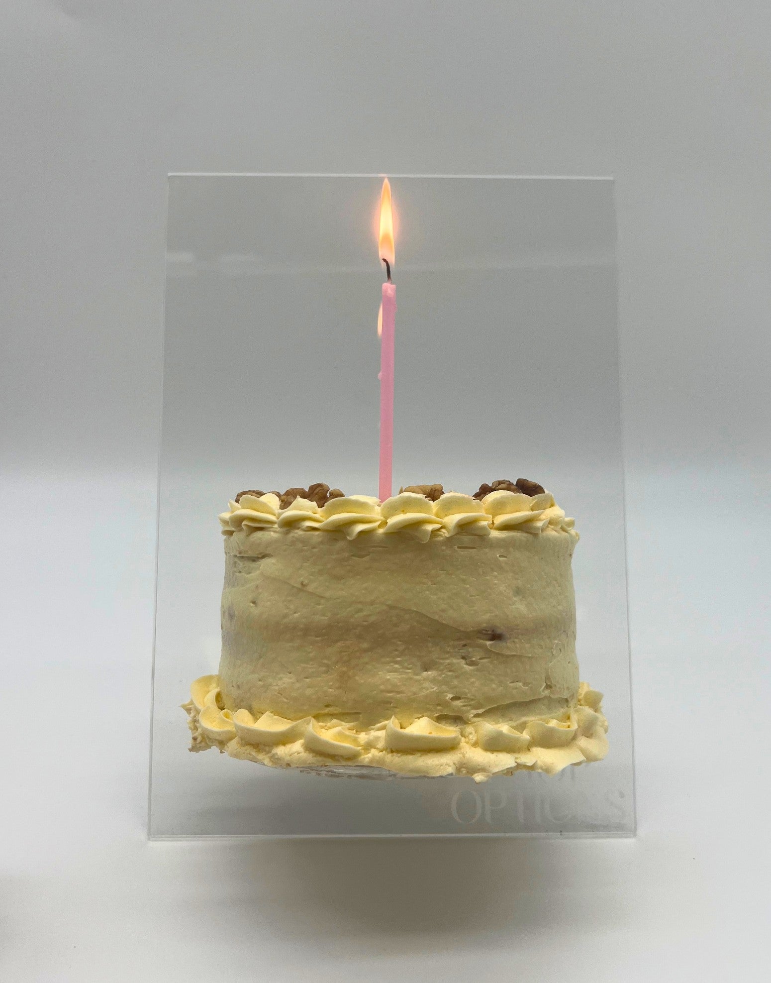 Clear acrylic cake easel stand for displaying decorated cakes, shown holding an 8-inch cake.