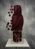 Personalised clear acrylic cake spacer set between dark burgundy draped fondant cake tiers