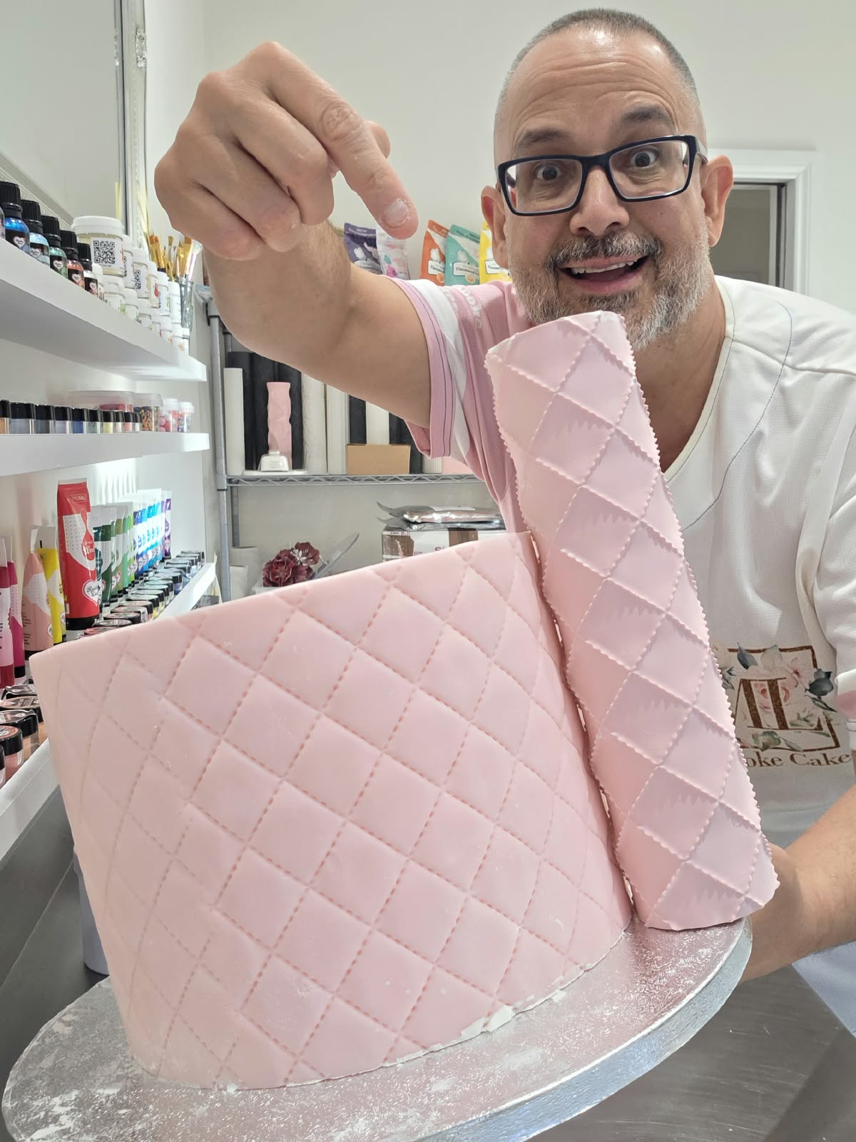Victor Diaz pointing at the Quilted diamond pattern rolled around a pink fondant cake with a rolled fondant sheet beside it - Prop Options